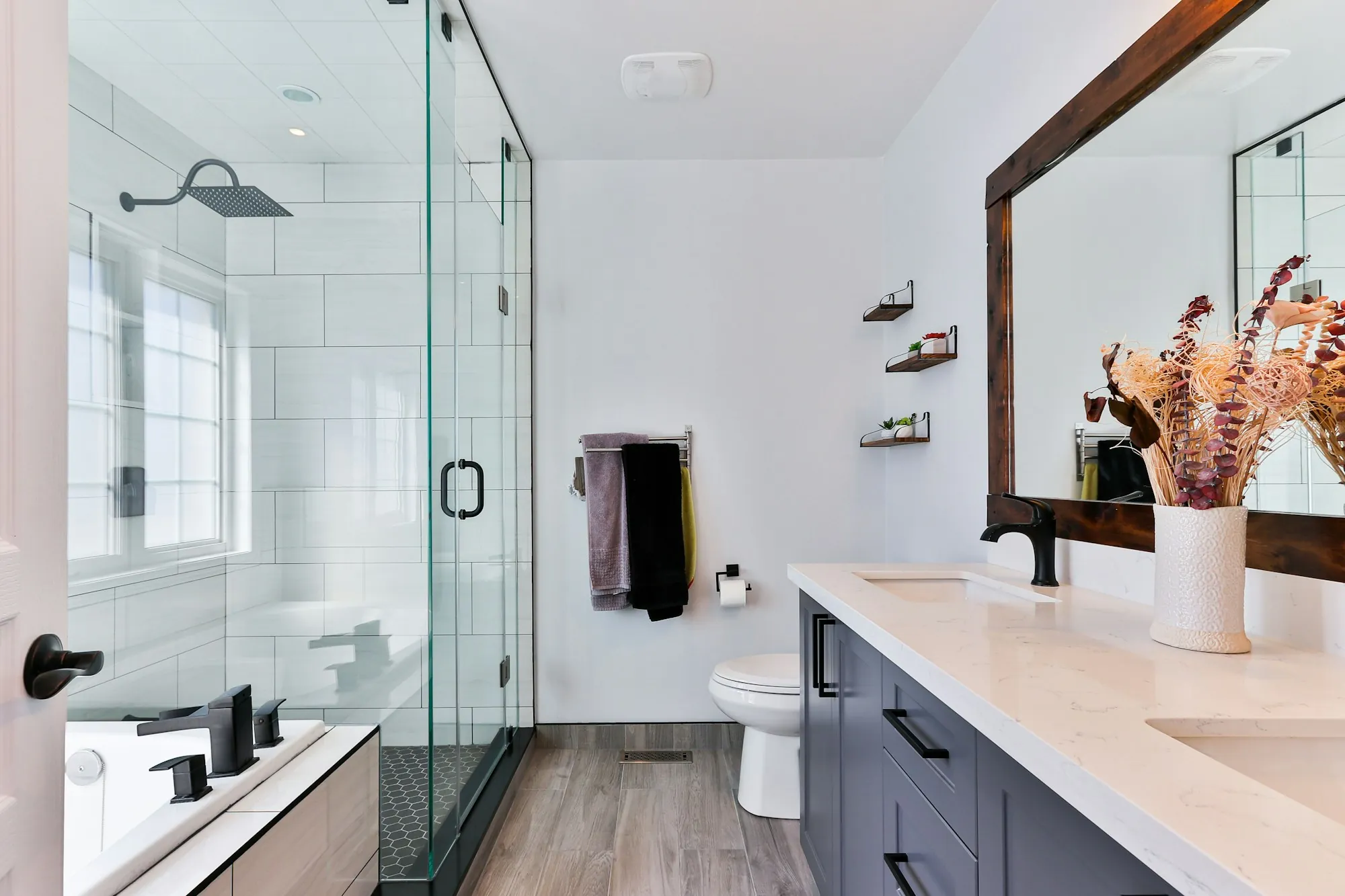 Remodeled bathroom with a frameless glass shower, white tile and a dark vanity