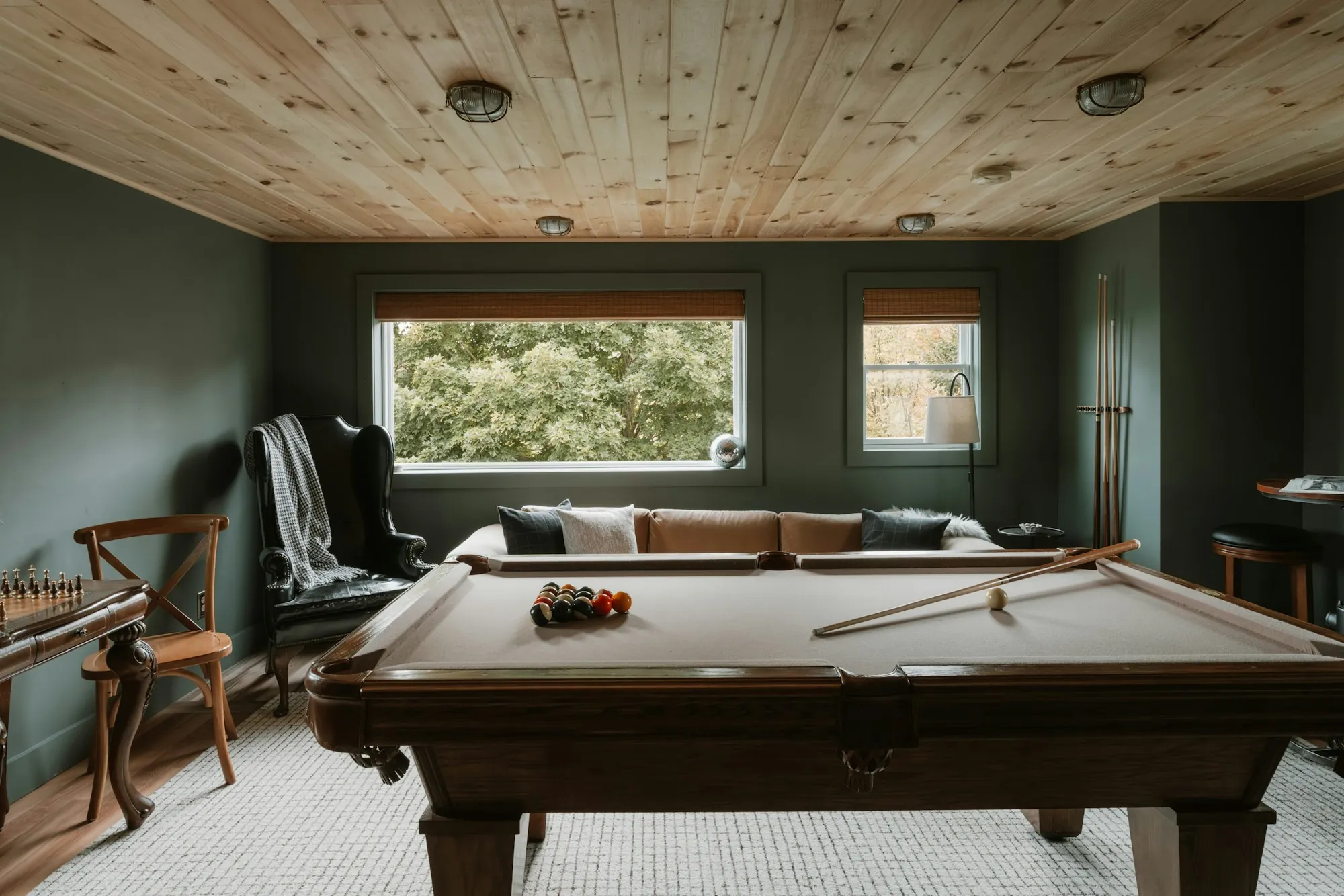 Finished lower-level game room with a pool table, wood plank ceiling and dark green walls