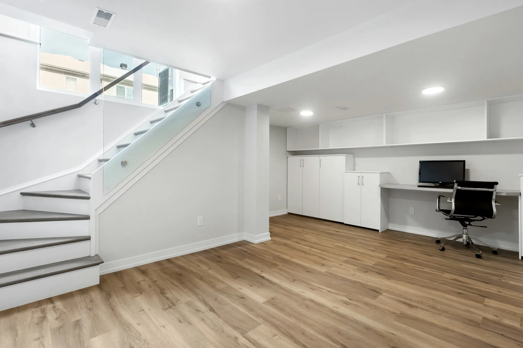 Finished basement with a glass-rail staircase, built-in desk and wood-look flooring