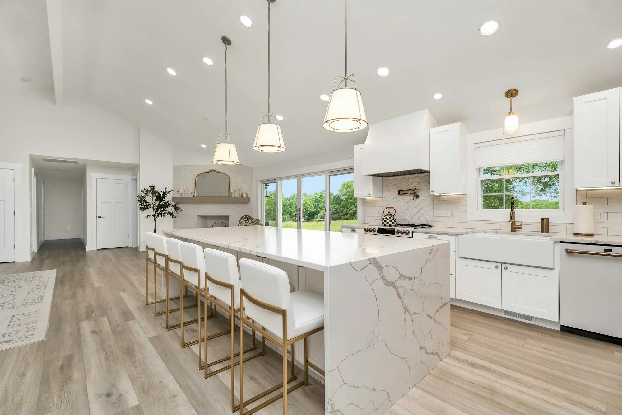 Remodeled white kitchen with a long marble waterfall island and a vaulted ceiling